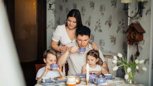 Contented family drinking tea with crepes together while sitting at table with candles at cozy kitchen with cuckoo clock on wall