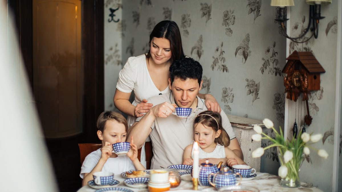 Contented family drinking tea with crepes together while sitting at table with candles at cozy kitchen with cuckoo clock on wall